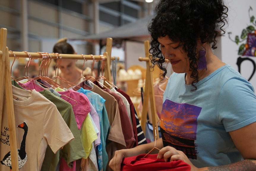 A woman at a market stall hanging up t-shirts.