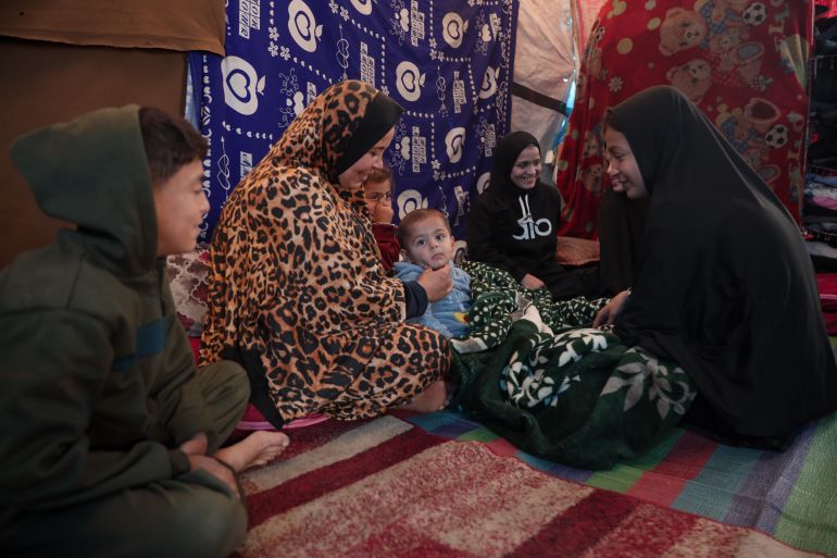 Sana’a sits with her children inside their tent, holding on to hope that living conditions will improve in the coming year [Abdelhakim Abu Riash/ Al Jazeera]