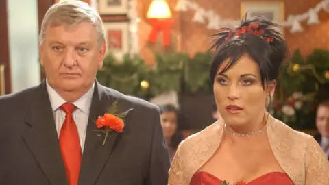 Derek Martin, in character as Charlie Slater, stands beside Jessie Wallace, in character as Kat Slater, in an episode of EastEnders.