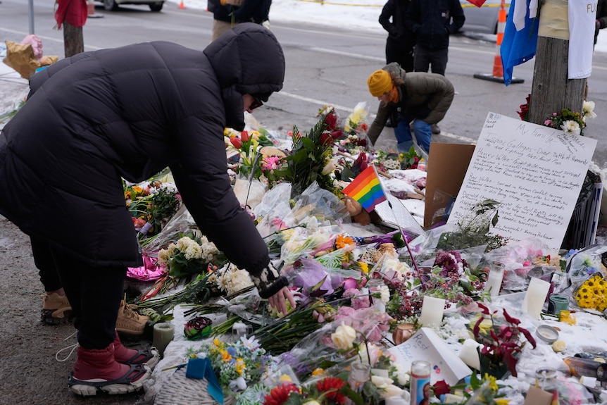 Several people place flowers down at a memorial for Renee Nicole Good.