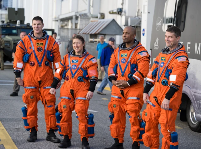 Four astronauts in orange suits, three are men and one is a woman.