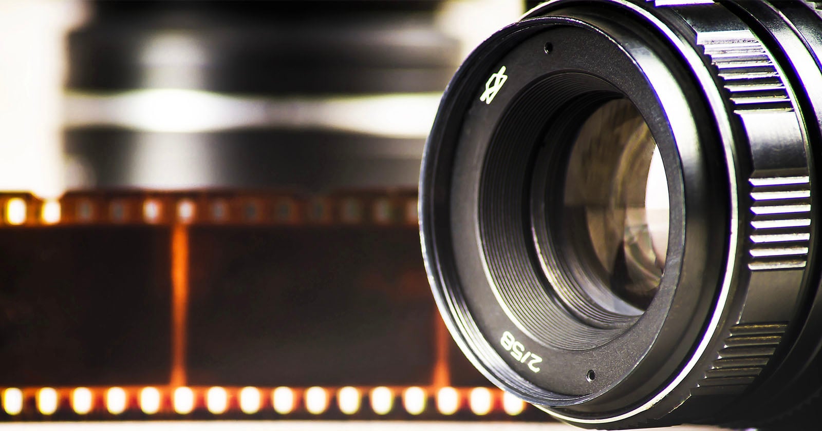 Close-up of a camera lens with a blurred film strip in the background, evoking a sense of photography and analog film.