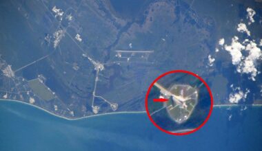 Aerial view of a coastal area with a space launch pad highlighted by a red circle and arrow, showing its location near the shoreline; surrounding land and water are visible.