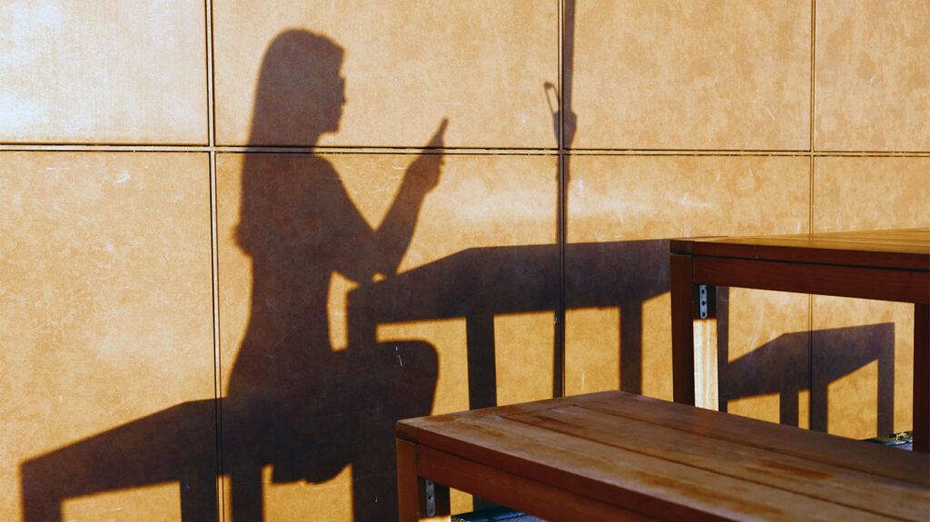 The shadow of a person using their smartphone.