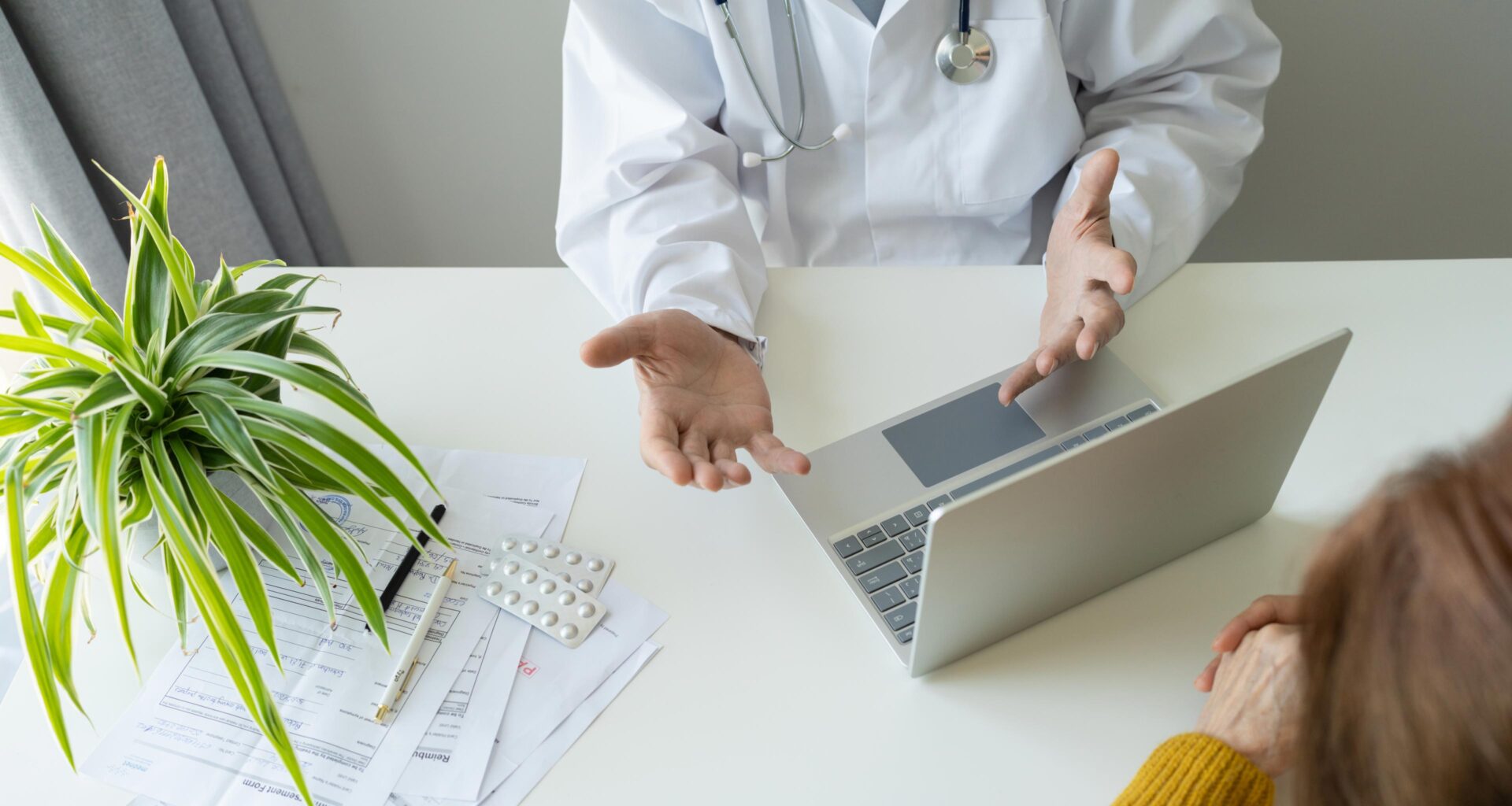 A doctor conversing with a patient. The doctor has a laptop in front of him.