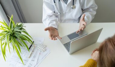 A doctor conversing with a patient. The doctor has a laptop in front of him.