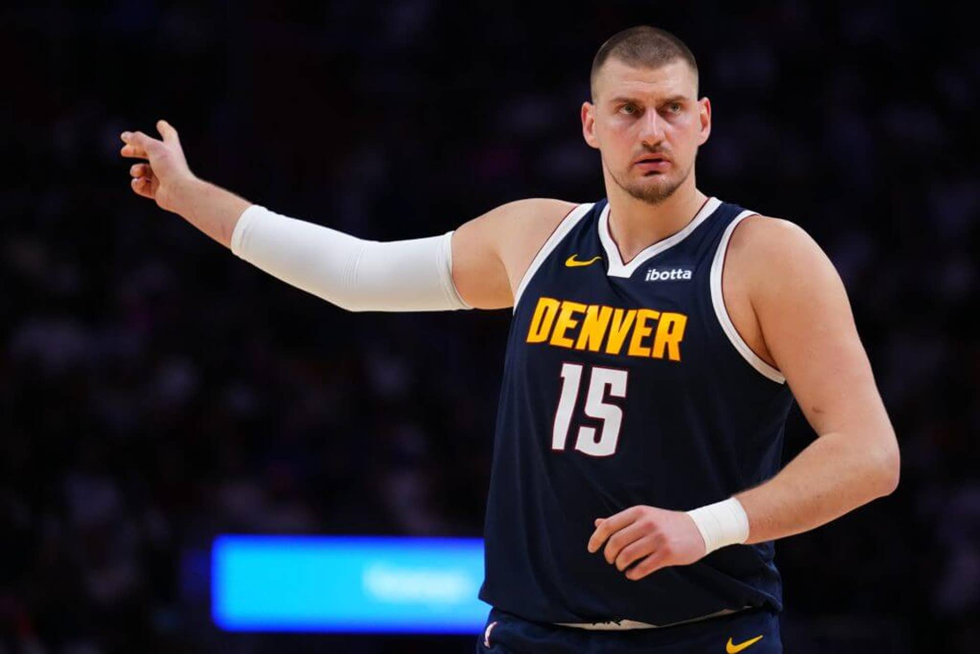 Nikola Jokić points behind him with his right hand.