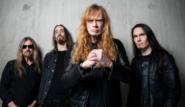 Megadeth standing against a grey backgroudn while Dave Mustaine holds his fist