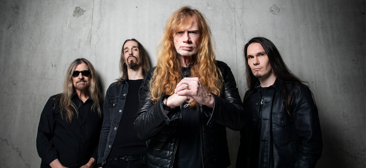 Megadeth standing against a grey backgroudn while Dave Mustaine holds his fist