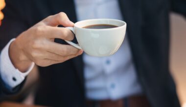 Close-up hand of young businessman in formal wear holding cup, mug of coffee