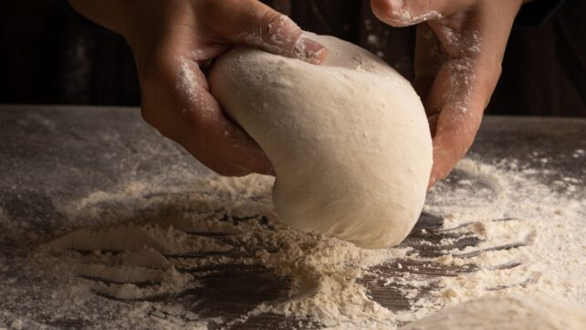 Hands rolling dough in flour