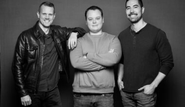 A grayscale photo of three men standing against a neutral background.