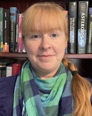 Young woman with long blonde bangs in front of a bookshelf.