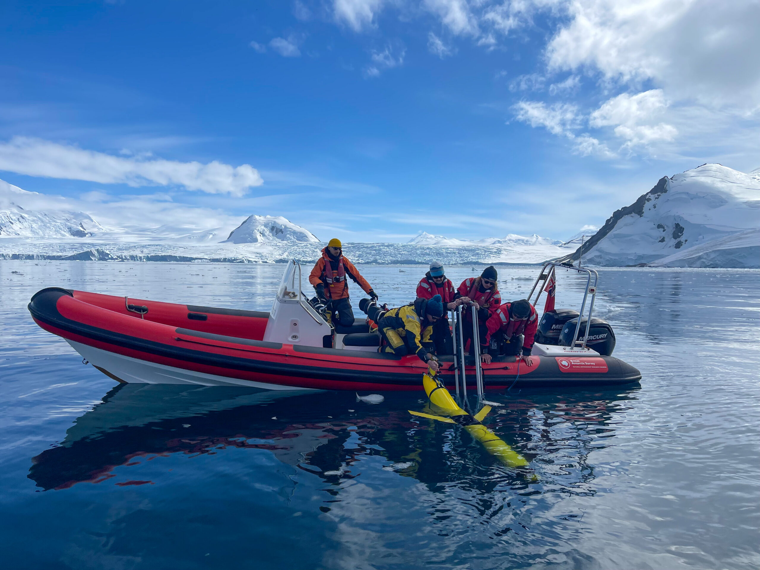 People on a small inflatable boat lowering a long yellow instrument into the ocean
