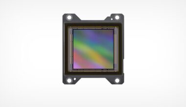 A close-up image of an electronic sensor, likely a camera sensor, with a rainbow-colored reflective surface and four mounting holes, set against a plain white background.