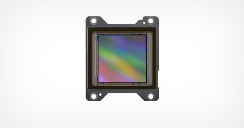 A close-up image of an electronic sensor, likely a camera sensor, with a rainbow-colored reflective surface and four mounting holes, set against a plain white background.