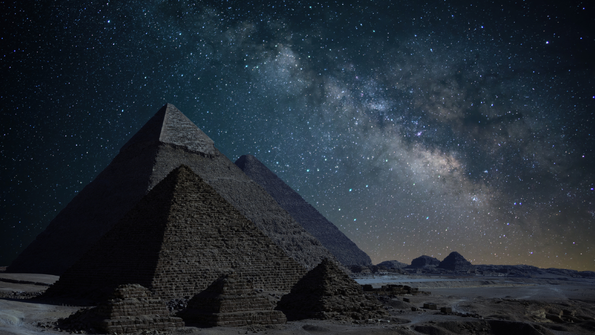 A series of brown pyramids against a rocky background with a starry blue night sky above.