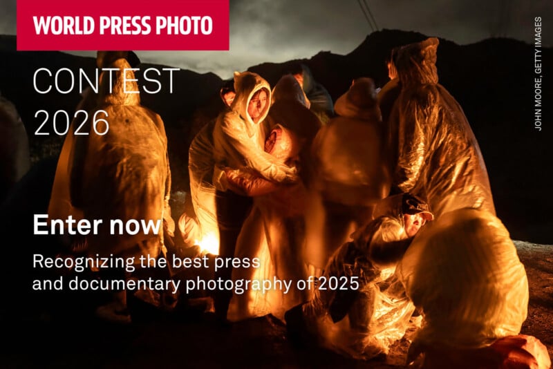 People in translucent plastic ponchos huddle closely together near a warm light at night. Mountains and dark skies are visible in the background. Text announces the World Press Photo Contest 2026 for press and documentary photography.