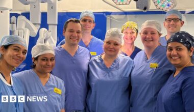 Donald Trump and Keir Starmer sit in a formal drawing room setting  on arm chairs with US and UK  flags behind them. Both have serious expressions and are looking out and not at each other.