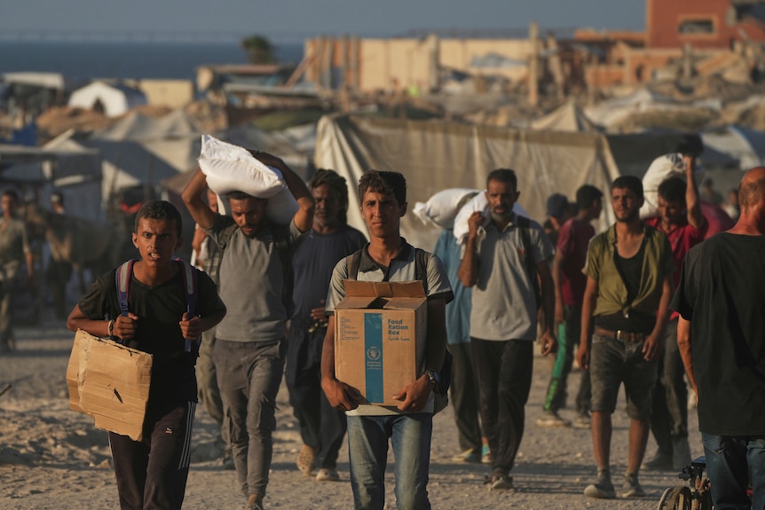 A Palestinian carries a box of food from the World Food Program with a group of other men.
