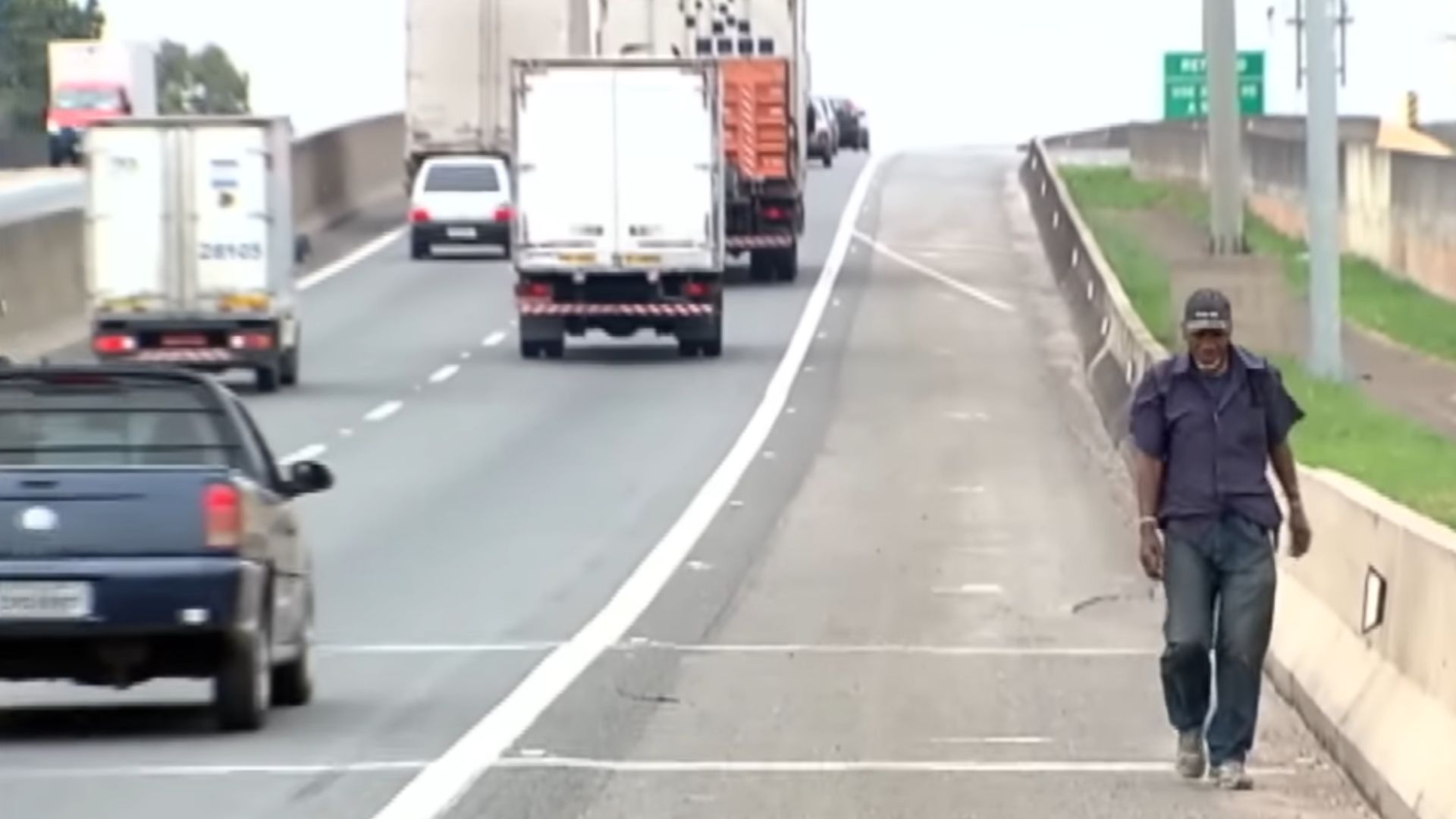 A wanderer walking alone along a Brazilian highway under a strong sun, with a backpack on his back.