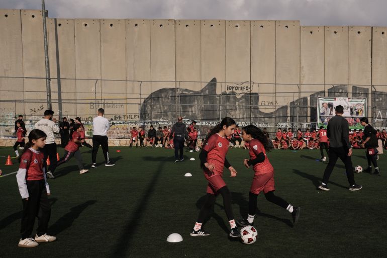 Palestinian girls and boys take part in a soccer practice session at a pitch next to Israel's separation wall in Aida Refugee camp, in the West Bank city of Bethlehem, Friday, Dec. 26, 2025, weeks after Israeli authorities issued a decision to demolish the field. (AP Photo/Mahmoud Illean)