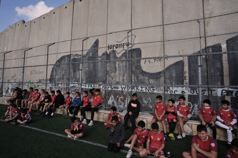 Palestinian youth attend a soccer practice session at a pitch next to Israel's separation wall in Aida Refugee camp, in the West Bank city of Bethlehem, Friday, Dec. 26, 2025, weeks after Israeli authorities issued a decision to demolish the field. (AP Photo/Mahmoud Illean)
