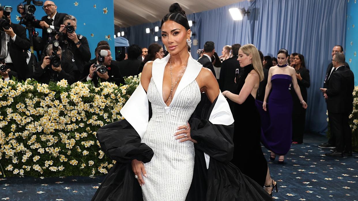 Nicole Scherzinger poses on the red carpet wearing a silver gown with photographers in the background.