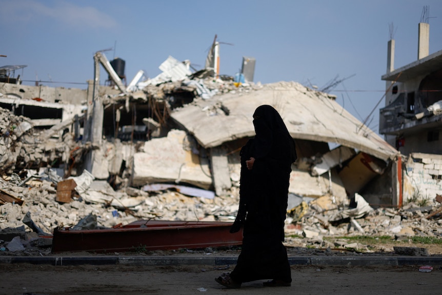 The silhouette of a woman walking through ruins in Gaza.