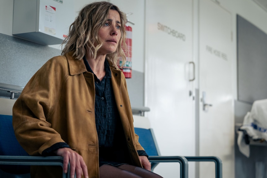 A TV still of Brooke Satchwell, 45, with chin-length blonde hair, looking distressed, while sitting in a chair in a hospital.