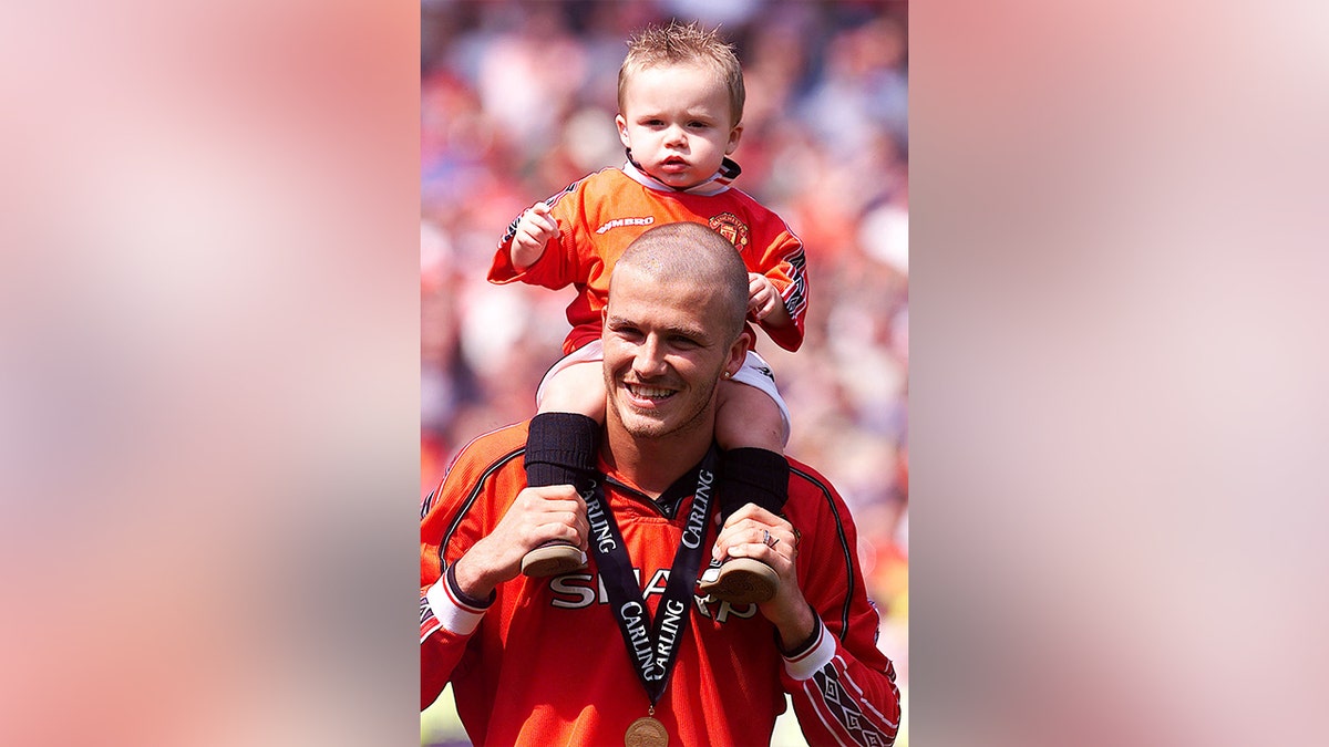 Brooklyn Beckham on his dad, David Beckham's shoulders ahead of a soccer match in England in 2000.
