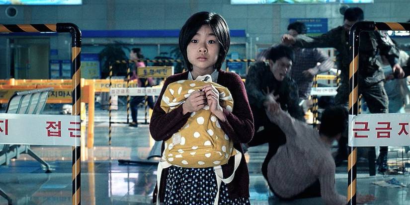 Soo-an, played by actor Kim Su-an, stands fearfully clutching a backpack while people fight behind her in Train to Busan.