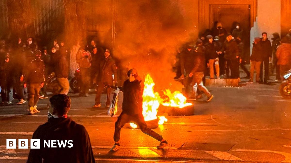 A screen grab of a video shows protesters standing near burning vehicles in the dark in Tehran, Iran.