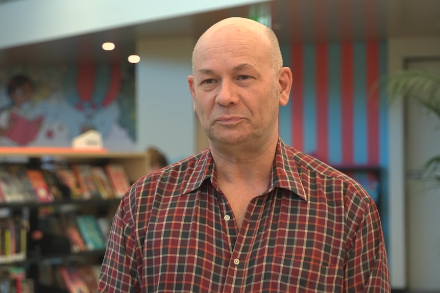 A man stands in front of bookshelves and a colourful wall