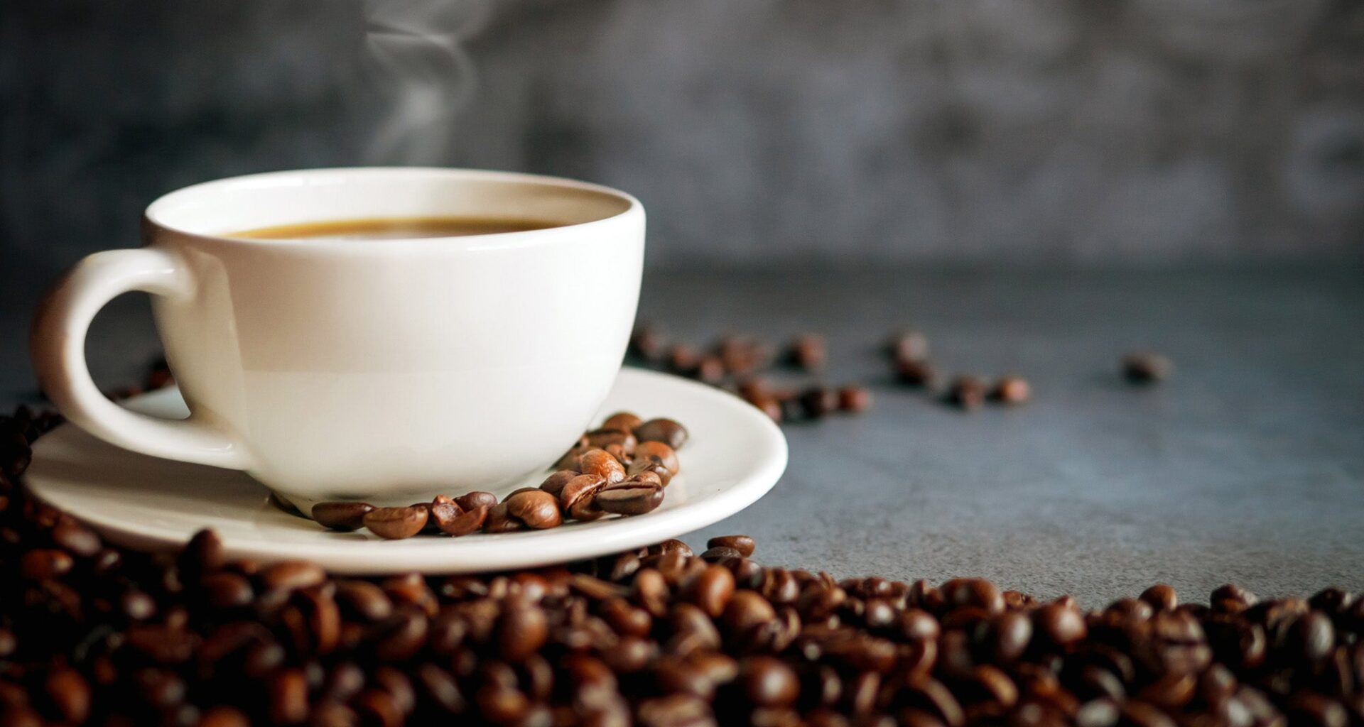 A steaming cup of coffee surrounded by coffee beans