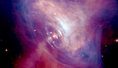 A red-and-blue image of a nebula is shown, shaped somewhat like an eye, with a plume of gas emitting from the center.