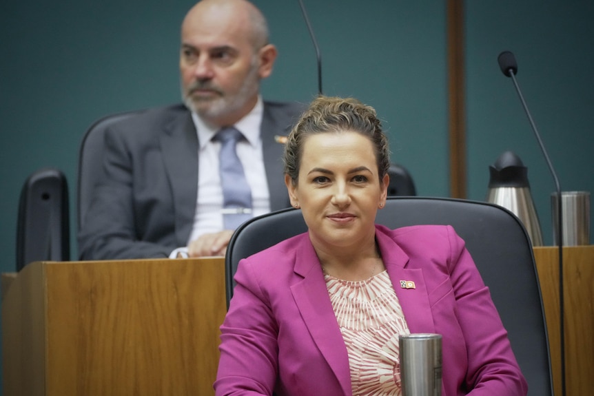 Woman in pink blazer sits in chair inside parliament