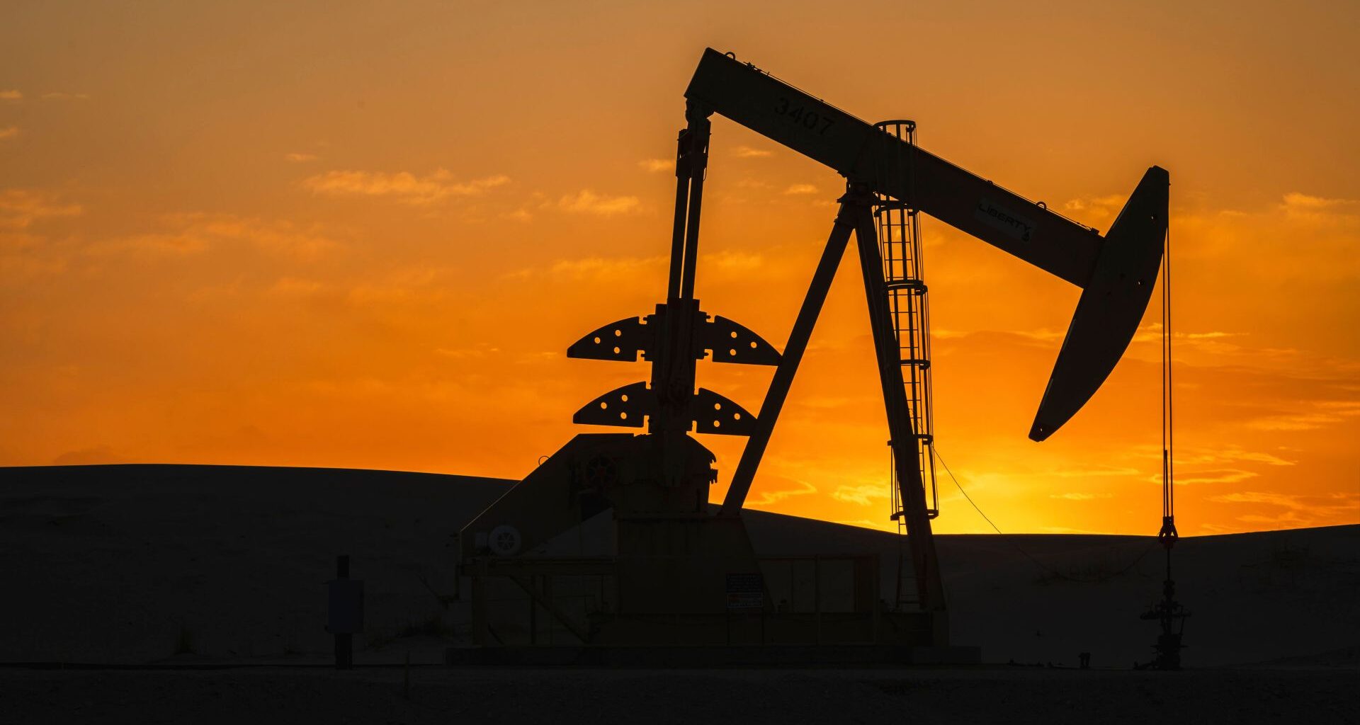 A silhouette of an oil drill sits in front of a orange and golden sunset