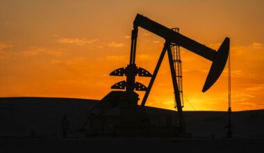 A silhouette of an oil drill sits in front of a orange and golden sunset