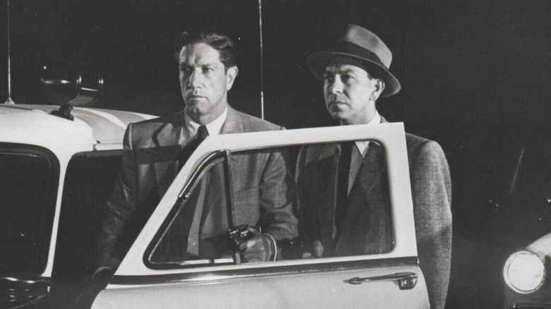 Sgt. Joe Friday stands by the door of a police car in Dragnet