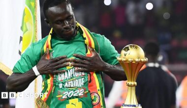 Sadio Mane holds his hands to his chest as he admires the Africa Cup of Nations trophy, which stands on a plinth
