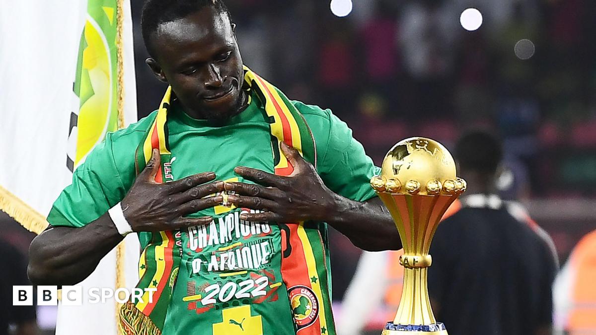 Sadio Mane holds his hands to his chest as he admires the Africa Cup of Nations trophy, which stands on a plinth