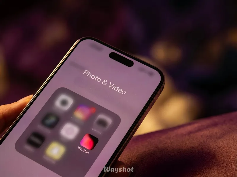 Close-up of a smartphone screen displaying a "Photo & Video" folder with blurred app icons, held in a hand with a purple background and soft lighting.