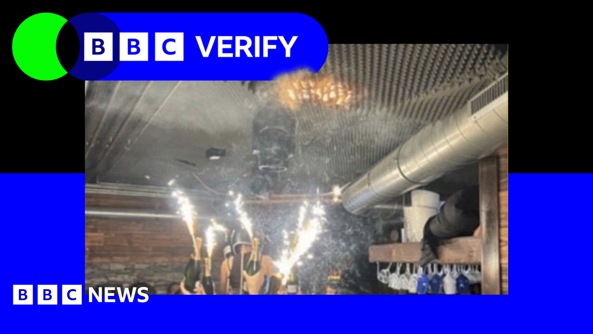 A branded image with the BBC Verify logo, with a blue border surrounding an image of sparklers attached to champagne bottles being held up by people in the Swiss ski resort bar just before the fire started - with a small orange patch of fire seen on a foam ceiling above the sparklers.