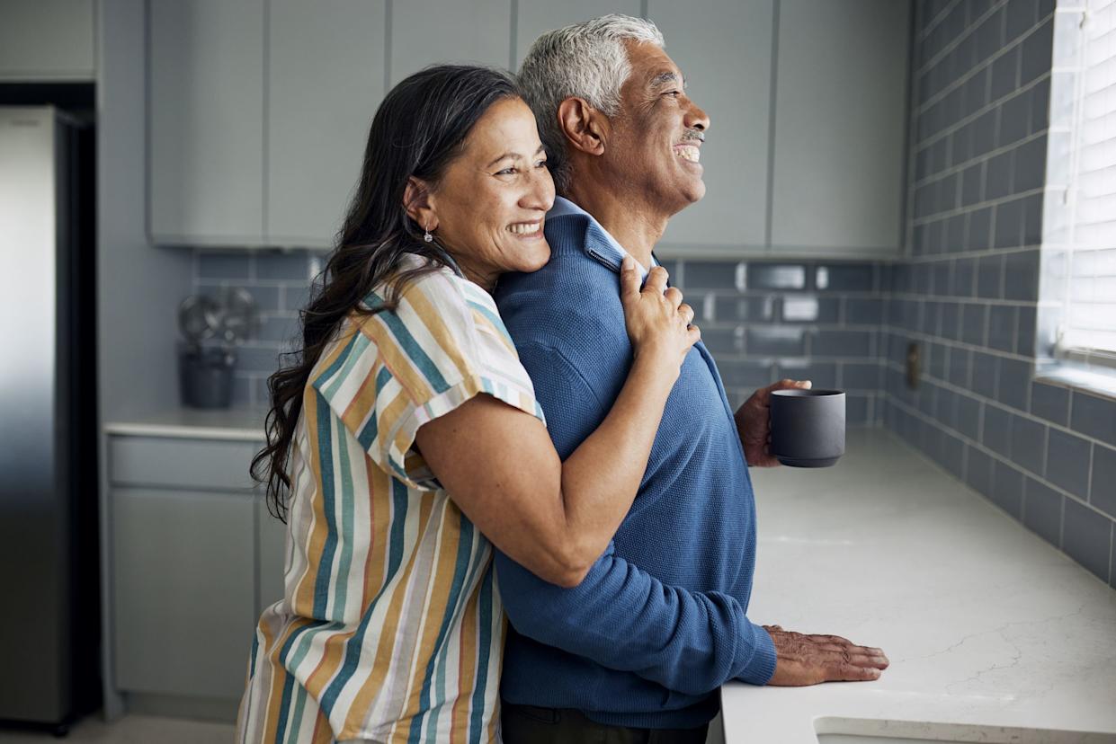 An elderly couple is drinking coffee and gazing out the kitchen window.