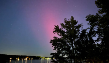 Blushing red and purple aurora over a light-lit body of water.