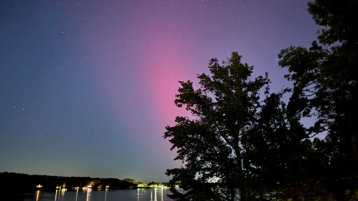 Blushing red and purple aurora over a light-lit body of water.