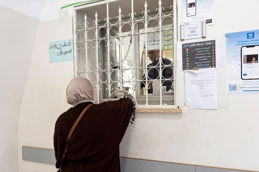A woman standing at a white counter, collecting medicine. 
