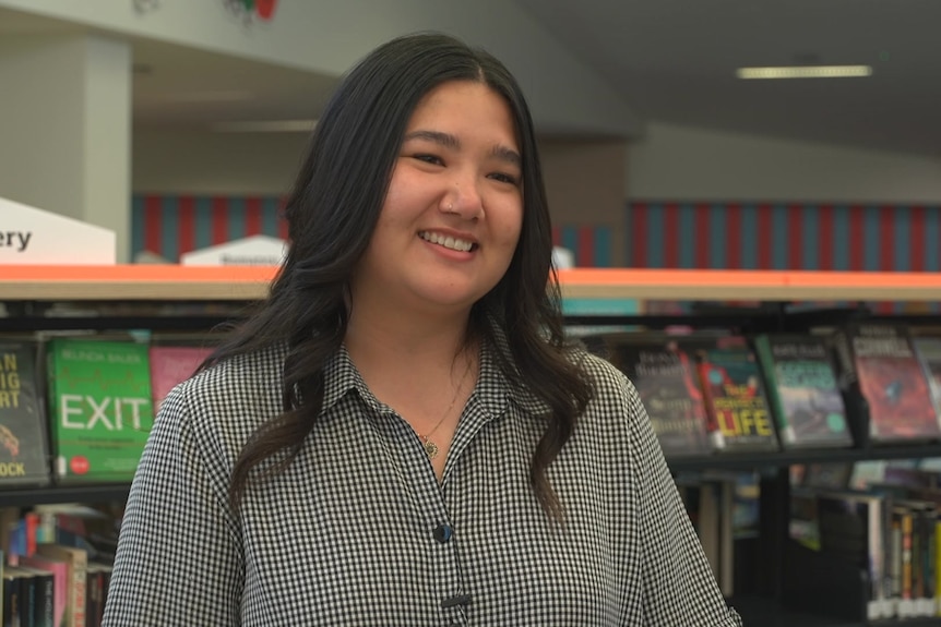 A woman smiles standing next to book shelves
