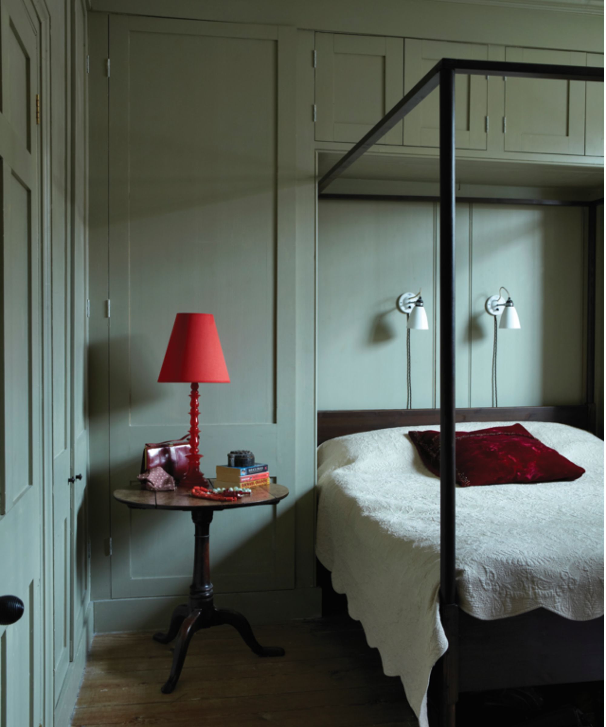 bedroom with color-drenched gray-green walls, a four-poster bed, and a bright red lamp on a side table
